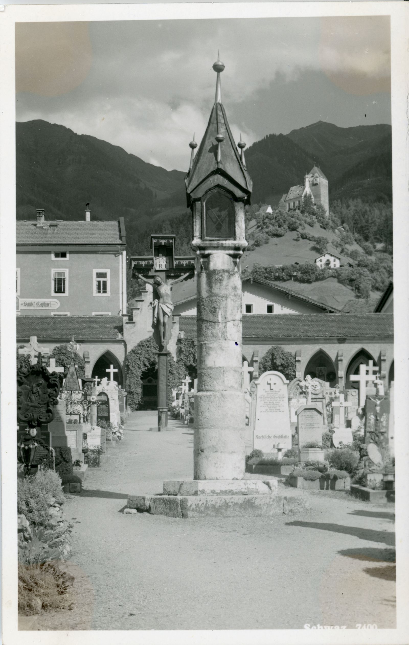 Friedhof mit Lichtsäule und Kruzifix dahinter. Im Hintergrund Freundsberg.